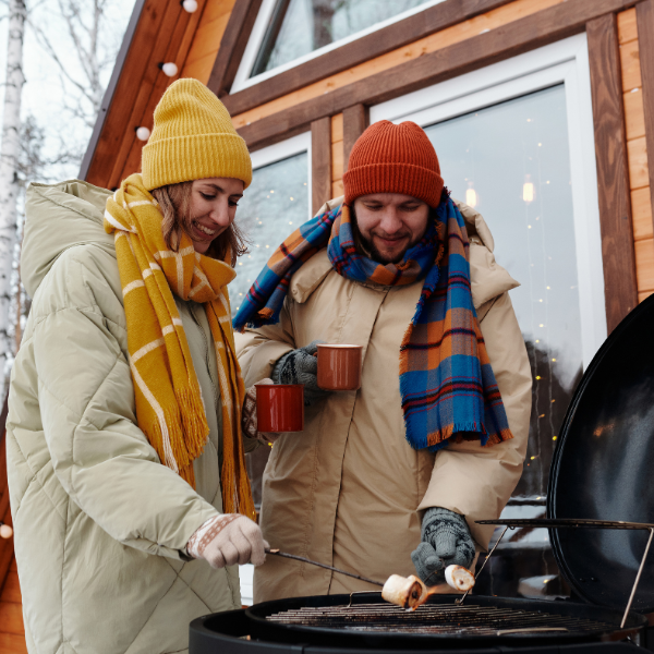 Stel geniet van een gezellige winter barbecue, gekleed in warme kleding, terwijl ze samen grillen in een besneeuwde tuin.